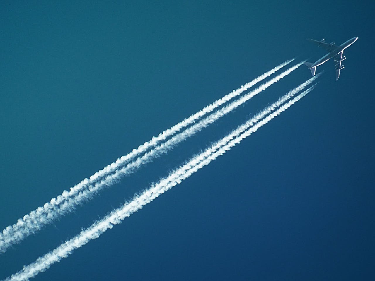 Aerial view of an airplane in flight, leaving vapor trails against a clear blue sky.