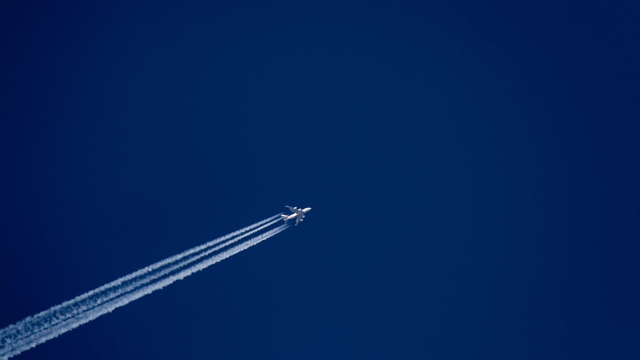 A high-flying airplane leaves distinct contrails against a clear blue sky, capturing the essence of flight.